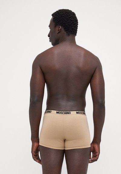 Beige boxer alsónadrág fekete 'MOSCHINO' derékkal, mely szoros illeszkedésű és puha anyagú, hátulról nézve.