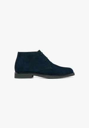Bottine en daim bleu marine avec deux œillets, bout rond, semelle noire et coutures minimales, montrée en profil latéral sur fond blanc.