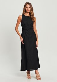Černé maxi šaty s bezramínkovou, přiléhavou horní částí a twist detailem v pase, plynule přecházející do volné sukně. Hladká tkanina, minimalistický design.