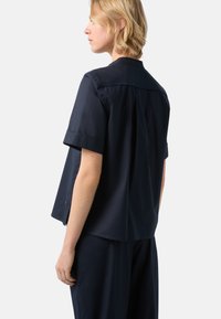 Navy short-sleeve shirt with a back yoke, side slits, and a relaxed fit. Made from a smooth, lightweight fabric.