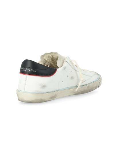 Scarpa sneaker bassa bianca con tallone nero, bordatura rossa, segni di usura visibili e lacci color crema, fotografata su uno sfondo bianco.