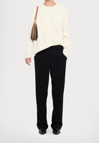 Pull crème côtelé, coupe décontractée, assorti à un pantalon noir taille haute. Accessoires comprenant un petit sac marron avec une sangle beige. Chaussures noires.