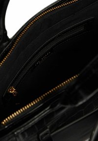 Sac à main en cuir noir avec motif crocodile, équipé d'une fermeture éclair dorée. L'intérieur comprend plusieurs poches, y compris un compartiment zippé et un revêtement en tissu doux.