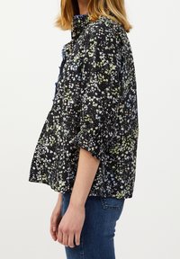 Blusa nera a fiori con maniche corte, caratterizzata da motivi floreali multicolori e dettagli arricciati nel colletto e nella parte anteriore.
