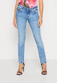 Light blue skinny jeans made of denim with a mid-rise waist, featuring front pockets and slight fading, paired with black heeled sandals.