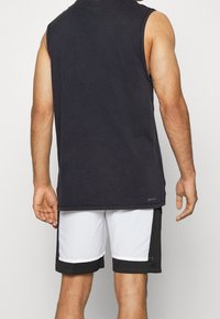 Maglietta nera senza maniche con scollatura rotonda, abbinata a pantaloni sportivi bianchi e neri con dettagli a contrasto.