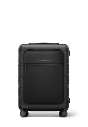 Valise rigide noire avec une finition texturée, une fermeture éclair lisse, une poche avant et quatre roues pour une mobilité aisée. Design compact.