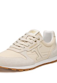 Scarpa sportiva beige in suede e pelle liscia, con lacci, colletto imbottito e accento del logo dorato sulla linguetta e sul lato.