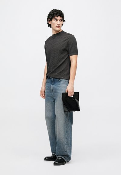 Čierna textúrovaná košeľa s krátkymi rukávmi, svetlomodré široké rifle a lesklá čierna taška s otvorom na držanie. Oblečenie dopĺňajú čierne topánky.