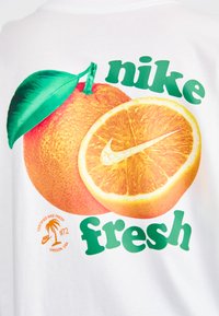 Balta marškinėliai su iliustracija apelsino ir pusiau perpjauto apelsino, su žaliais užrašais "nike" ir "fresh". Kampelyje yra logotipas.