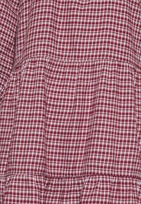 Tissu à carreaux rouge et blanc en vichy, présentant un motif à damiers, avec un détail de couture froncée et une surface texturée.