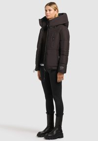 Črna puffer jakna z visokim ovratnikom, zadrgo spredaj in rebrastimi rokavi. Ima stranske žepke in spodnji del s šnokcem. Ujemanje s črnimi leggingi in debelimi škornji.