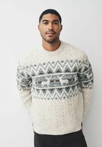 Cremefarbener Pullover mit strukturiertem Strick, geometrischen Mustern und Hirschmotiven in Grau und Braun. Rundhalsausschnitt und gerippte Bündchen sowie Saum.