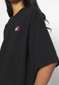 Svart oversized t-shirt i bomull, med en liten broderad Tommy Jeans-logotyp i röd, vit och blå färg på vänster bröst.