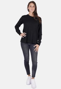 Maglietta nera a maniche lunghe con scollo rotondo, indossata con jeans attillati scuri e sneakers bianche. Design semplice, tessuto morbido e senza motivi visibili.