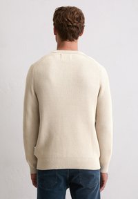 Strickpullover in Off-White, strukturiertem Stoff mit gerippten Bündchen und Saum. Mit rundem Halsausschnitt und seitlichem Etikettenteil.