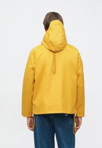 Gul vannavstøtende jakke med hette, med glatt tekstur, justerbare snorer og en avslappet passform. Bakside har minimal detaljering.