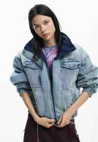 Jachetă de denim în albastru deschis, cu guler interior bleumarin, având două buzunare pe piept, manșete elastice și fermoar frontal. Evidențiată printr-o croială conică.