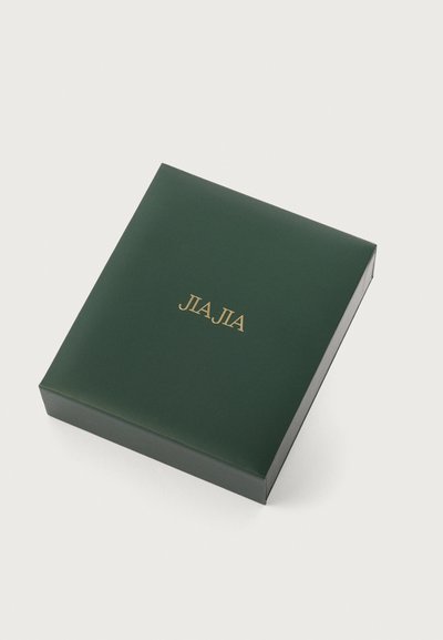 Tamsiai žalia kvadratinė dėžutė su blizgiu paviršiumi, viršuje yra aukso spalvos užrašas "JIA JIA".