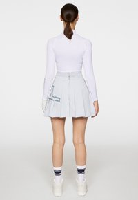 Jasnoniebieska plisowana spódnica z wysokim stanem, zestawiona z dopasowaną białą bluzką z długim rękawem. Białe sneakersy i wzorzyste skarpetki dopełniają stylizację.