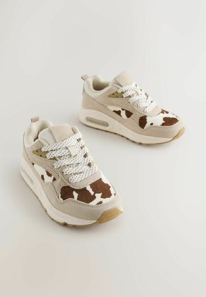 Beiget tennarit, joissa lehmäkuvioiset yksityiskohdat, teksturoitu mokkanahka ja verkkomateriaalit, valkoiset nauhat ja vaaleanruskea kumipohja, jossa on ilmatyynyt.