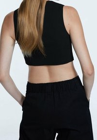 Svart crop top med en figurnära design, rundad halsringning och utan ärmar, kombinerad med svarta byxor med elastisk midja. Mjuk textur, minimalistisk stil.