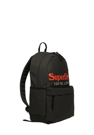 Mochila negra SuperDry con texto de logo en rojo y blanco, correas de hombro acolchadas, bolsillo frontal con cremallera y asa superior para llevar.