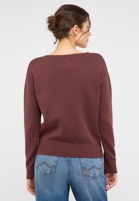 Burgunderfarbener Strickpullover mit strukturiertem Saum und Bündchen, in lässigem Schnitt und weitem Ausschnitt, kombiniert mit hellblauen Jeans.