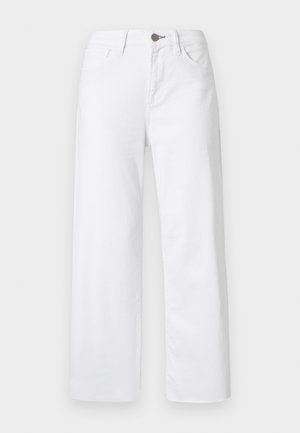 Rode kortärmelig t-shirt en witte broek met wijde pijpen. Het model houdt een lichtblauw accessoire vast. Zwarte schoenen met hak maken de look compleet.