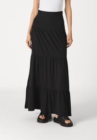Svart, tiered maxi-skjørt laget av mykt stoff med elastisk midje. Kombinert med kraftige svarte slip-on sandaler.