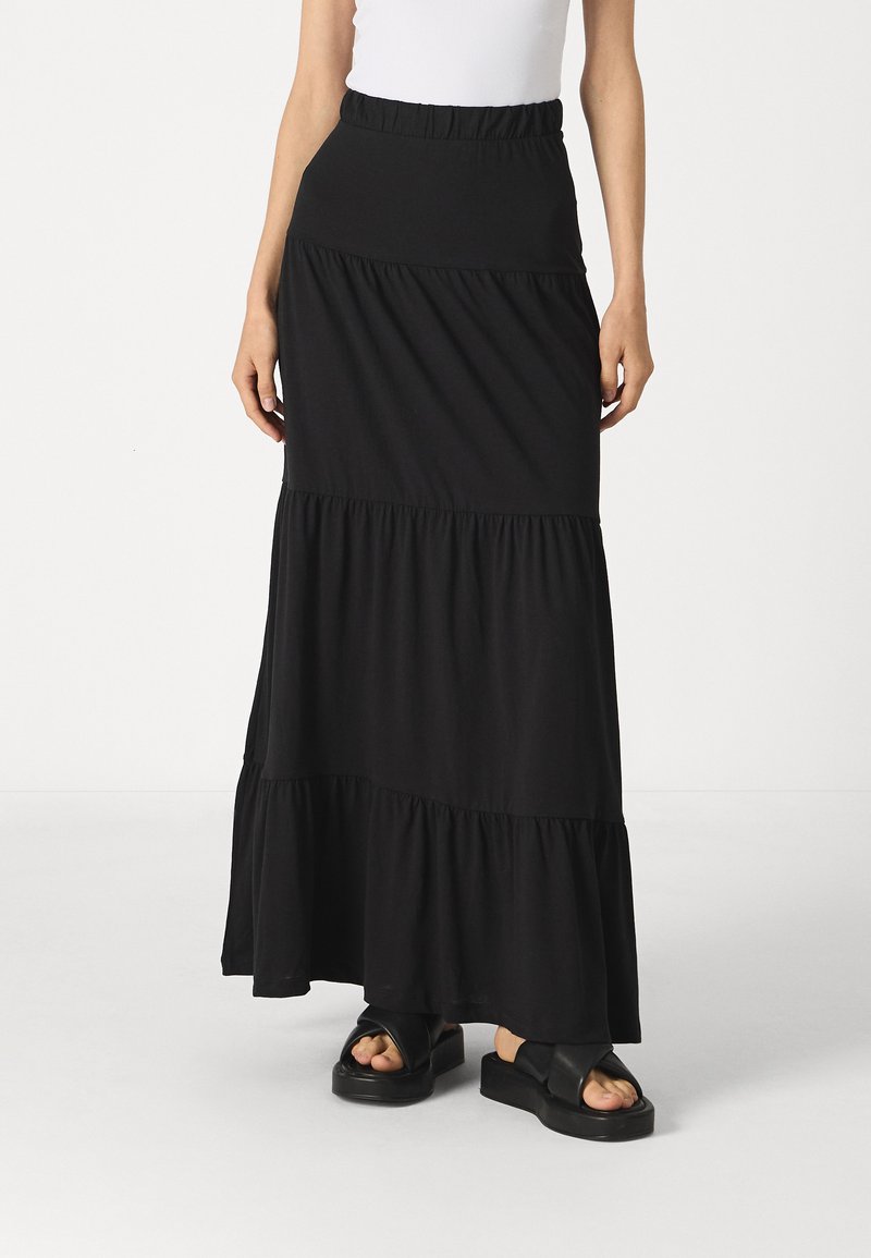 Svart, tiered maxi-skjørt laget av mykt stoff med elastisk midje. Kombinert med kraftige svarte slip-on sandaler.