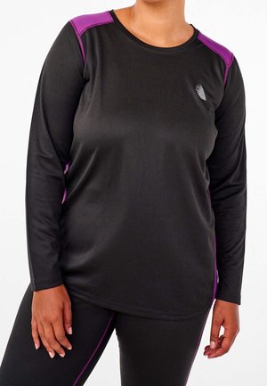 Frau trägt ein langärmeliges schwarzes Sportoberteil mit violetten Schulterakzenten und passende schwarze Leggings mit violetten Seitenstreifen.