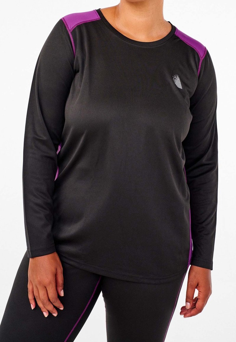 Femme portant un haut de sport noir à manches longues avec des accents violets aux épaules et des leggings noirs assortis avec des bandes latérales violettes.