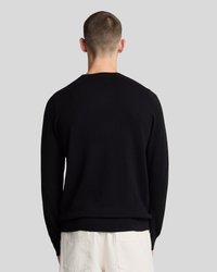 Pull en tricot noir avec un col rond, des manches longues et une coupe décontractée. Texture lisse avec des poignets et un ourlet côtes.
