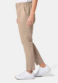 Pantalons beiges ajustés avec une taille élastique, poches latérales et un ourlet fendu. Assortis à des baskets blanches pour un look décontracté.