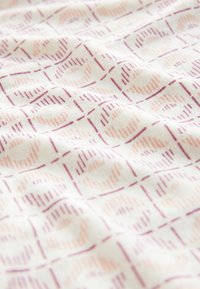 Pamut szövet pasztell rózsaszín és lila színű, egymásba fonódó körök geometriai mintájával világos krémszínű háttéren.