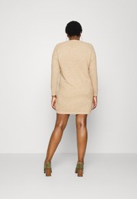 Robe pull beige tricotée à manches longues, avec un col rond et une texture côtelée, associée à des chaussures vertes à talons hauts.