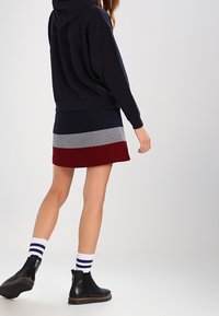 Sudadera marinera de corte holgado, combinada con una falda bloqueada en colores azul marino, gris y burdeos; botas negras hasta el tobillo y calcetines blancos a rayas.