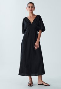 Black linen maxi dress with a V-neckline and puff sleeves, featuring gathered detailing at the waist and a flowing silhouette.