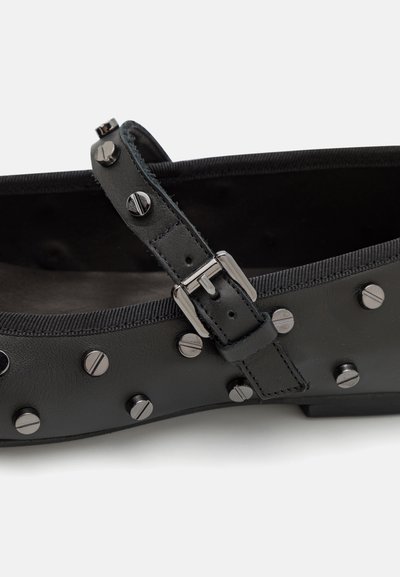 Chaussure plate noire en cuir, dotée d'une sangle avec une boucle métallique et des clous décoratifs argentés. Intérieur texturé avec un revêtement gris.
