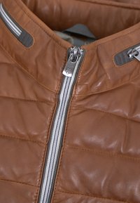 Braune Lederjacke mit gestepptem Muster, ausgestattet mit einem silbernen Reißverschluss und grauen Akzenten am Kragen und im Bereich des Reißverschlusses.