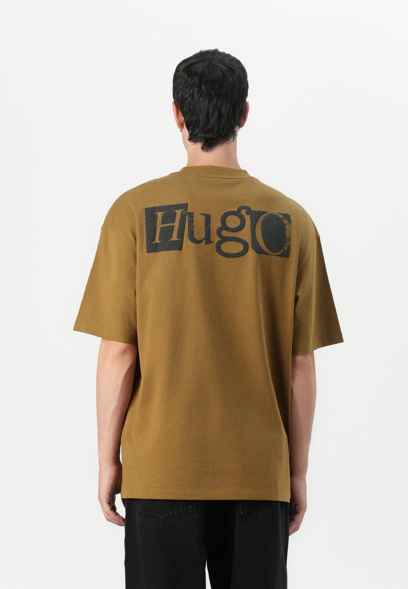 Bruine katoenen t-shirt met korte mouwen. Beschikt over een groot zwart "Hugo" logo op de achterkant. Rechte zoom; ontspannen pasvorm. Geen zichtbare patronen of accenten.