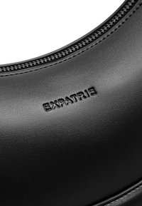 Borsa in pelle sintetica nera con finitura testurizzata, caratterizzata da una chiusura con cerniera e logo "EXPATRIE" in rilievo sulla superficie.