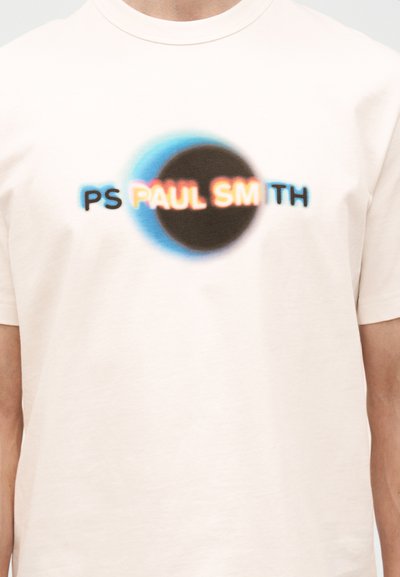 Hvit T-skjorte med en svart sirkel omgitt av et blått skjær, med uskarp tekst "PS PAUL SMITH" over brystet.