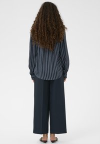 Tumši zila garām piedurknēm svītraina krekls ar noapaļotu apakšu, kopā ar platām tumši ziliem biksēm. Audums šķiet gluds un siluets atslābināts.