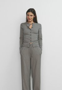 Conjunto de ropa de descanso a rayas en blanco y negro; parte superior de manga larga con botones y escote curvado, combinada con pantalones de cintura ajustable con cordón.