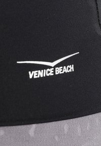 Černé sportovní oblečení s nápisem "VENICE BEACH" ve bílé barvě. Tkanina má žebrovanou strukturu, pod ní je hladká šedá část.