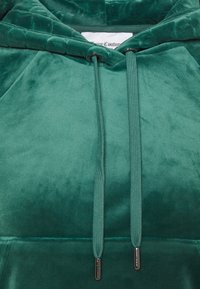 Hoodie in velluto verde con una texture liscia, cordini con punte in metallo e un sottile motivo impresso sul cappuccio.