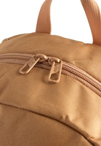 Mochila de tela marrón con un exterior texturizado, que cuenta con un cierre de doble cremallera y un asa corta de tela. El herraje tiene un acabado mate.