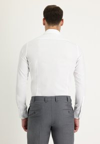Camisa blanca de manga larga con cuello clásico, combinada con pantalones grises de corte entallado que cuentan con una textura sutil y detalles de bolsillo trasero.